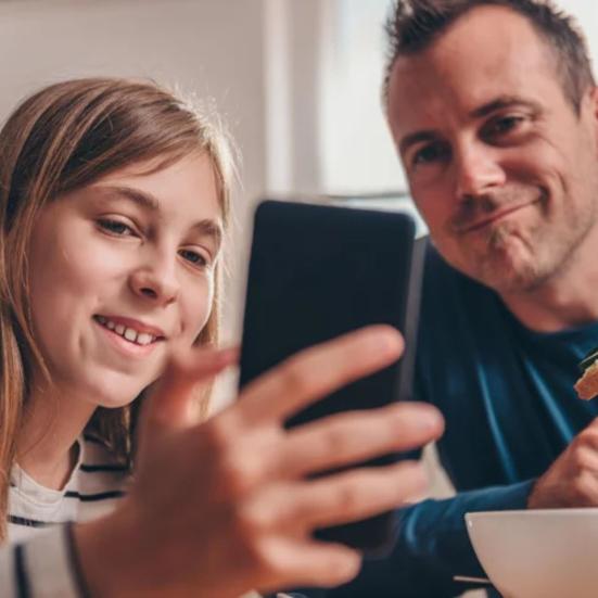 Pige kigger på mobiltelefon og far kigger med