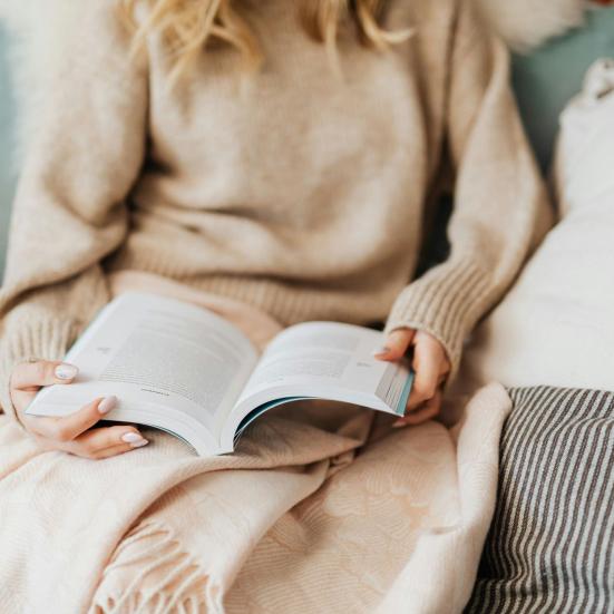 Kvinde læser i sofaen med et tæppe over sig.